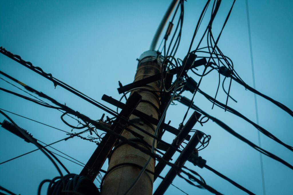 The top of a telephone pole with many wires viewed from the base.