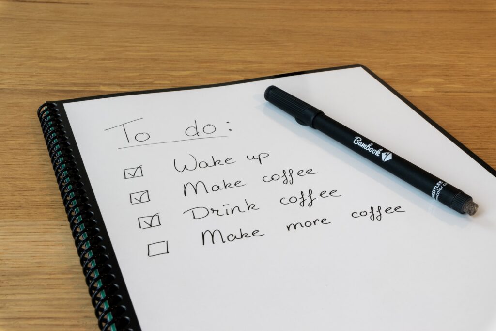 A pen lying on a piece of paper with a checklist that says to do: Wake up Make coffee Drink coffee Make more coffee