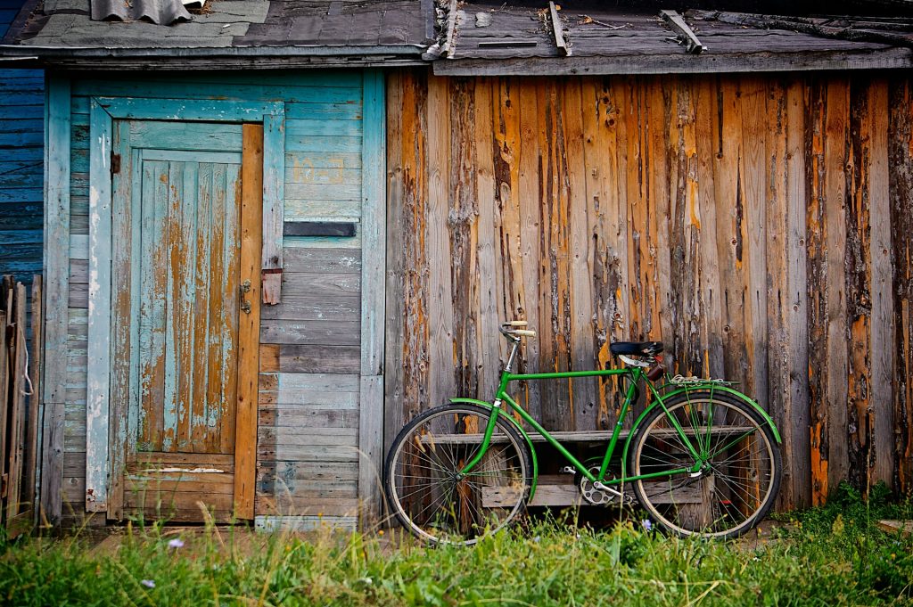 A green bicycle leaning against a wooden shed. The shed's paint is mostly gone. What remains is a faded turquoise.