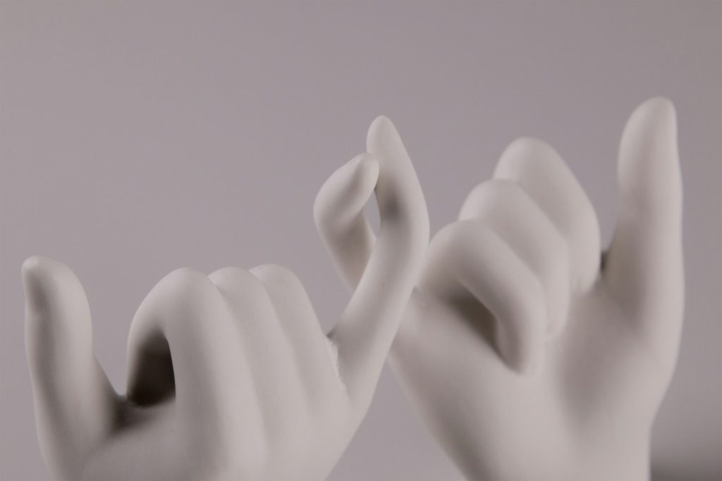 Two white sculpted hands arranged in a pinky promise