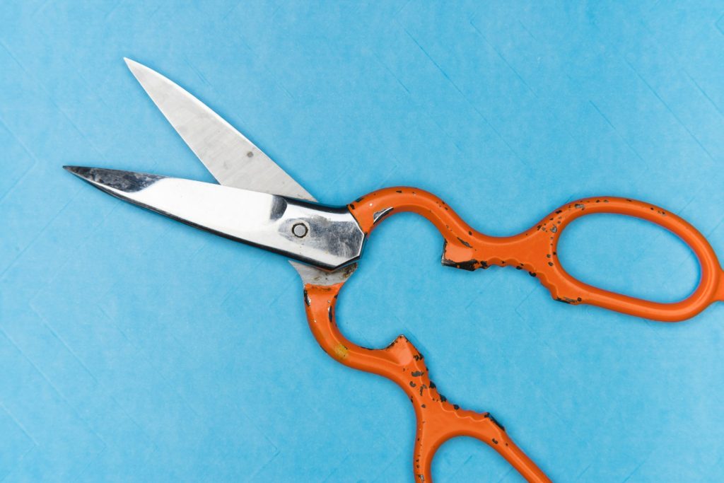 Metal scissors with orange handles on a light blue background.