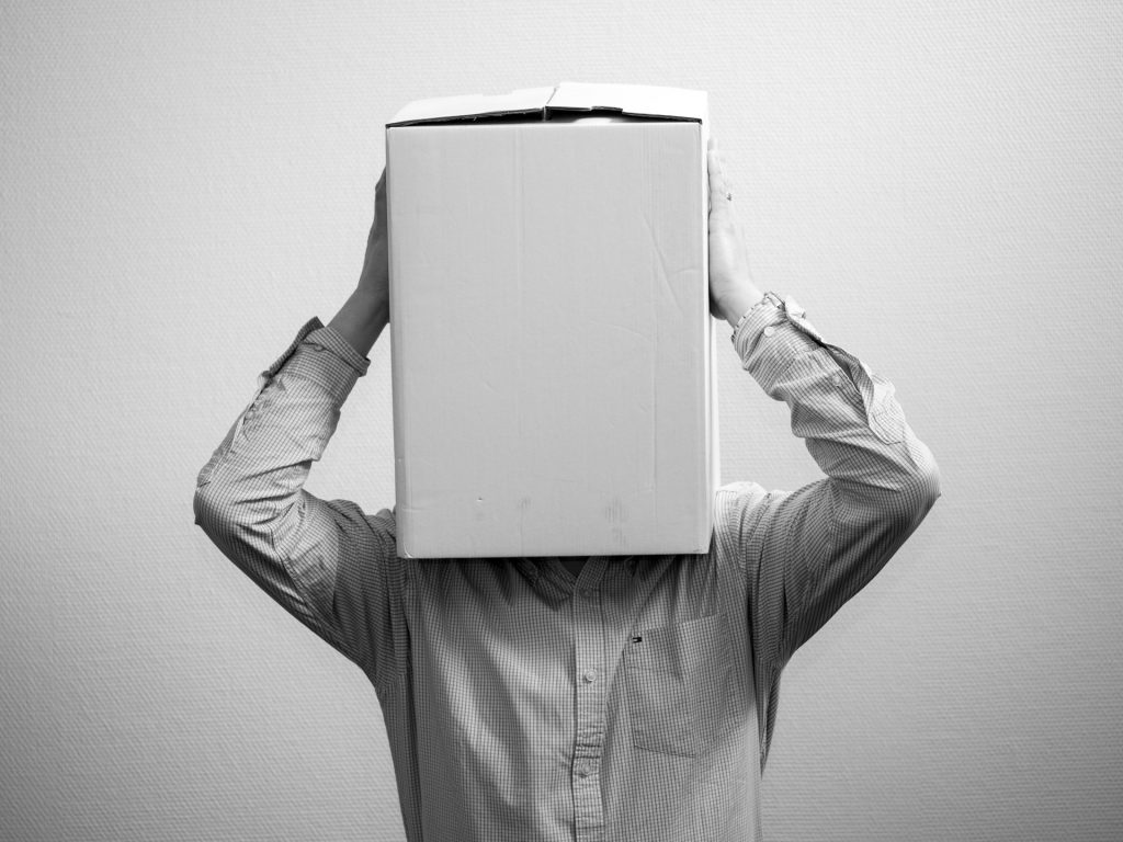 A black and white photo of a person covering their head with a cardboard box.